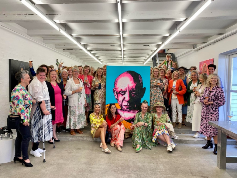 Group Exhibition Celebration at Galerie Wolfsen - Aalborg 2024 A large group of women posing in colorful dresses around a vibrant portrait artwork at Galerie Wolfsen in Aalborg, Denmark.